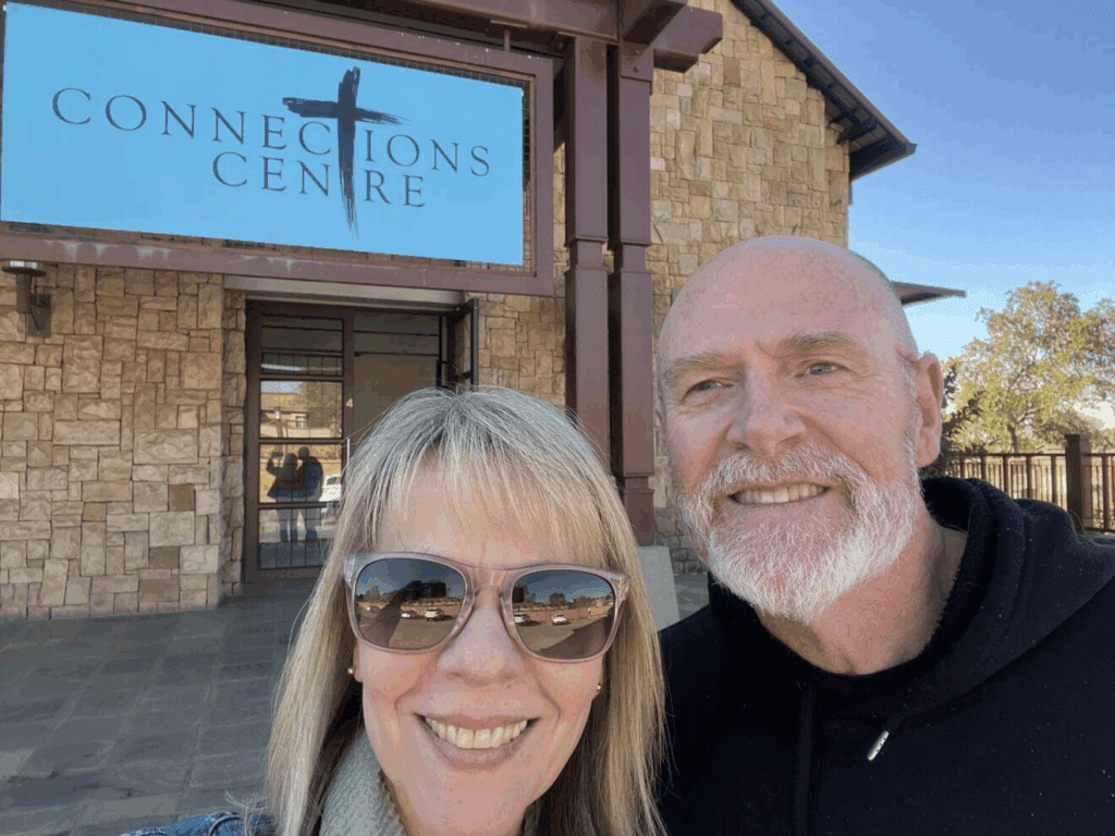 A man and woman pose together in front of a building labeled "Connections Centre."